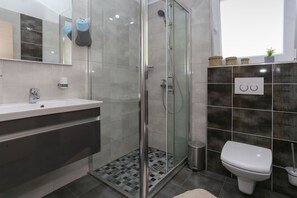 A modern bathroom with a glass-enclosed shower, a white sink, and a toilet. - Apartments Bruno (Okrug)