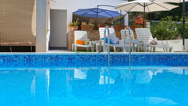 A clear blue pool with lounge chairs and umbrellas. - Apartments Bruno (Okrug)