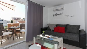 A modern living room with a glass coffee table, grey sofa, and a red pillow. - Apartments Bruno (Okrug)