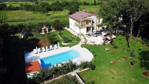 Une maison à deux étages avec une piscine, entourée d’un jardin bien entretenu et de vignobles.