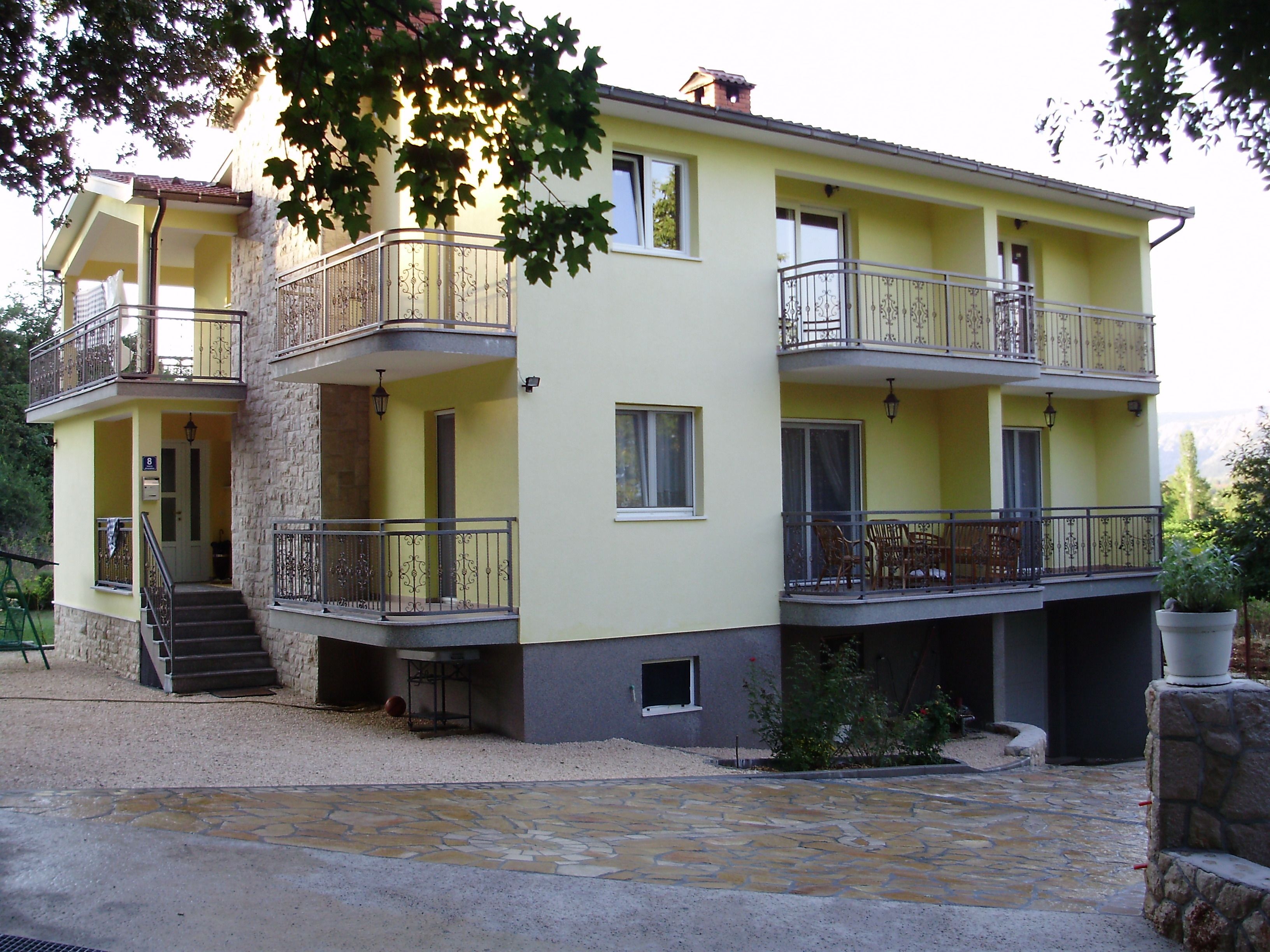 A two-story building with balconies, a stone staircase, and a gravel driveway.