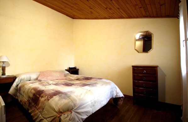 Ein Schlafzimmer mit Holzbalkendecke, einem Bett mit Quilzudecke, einem Schminktisch und einem Spiegel an der Wand.