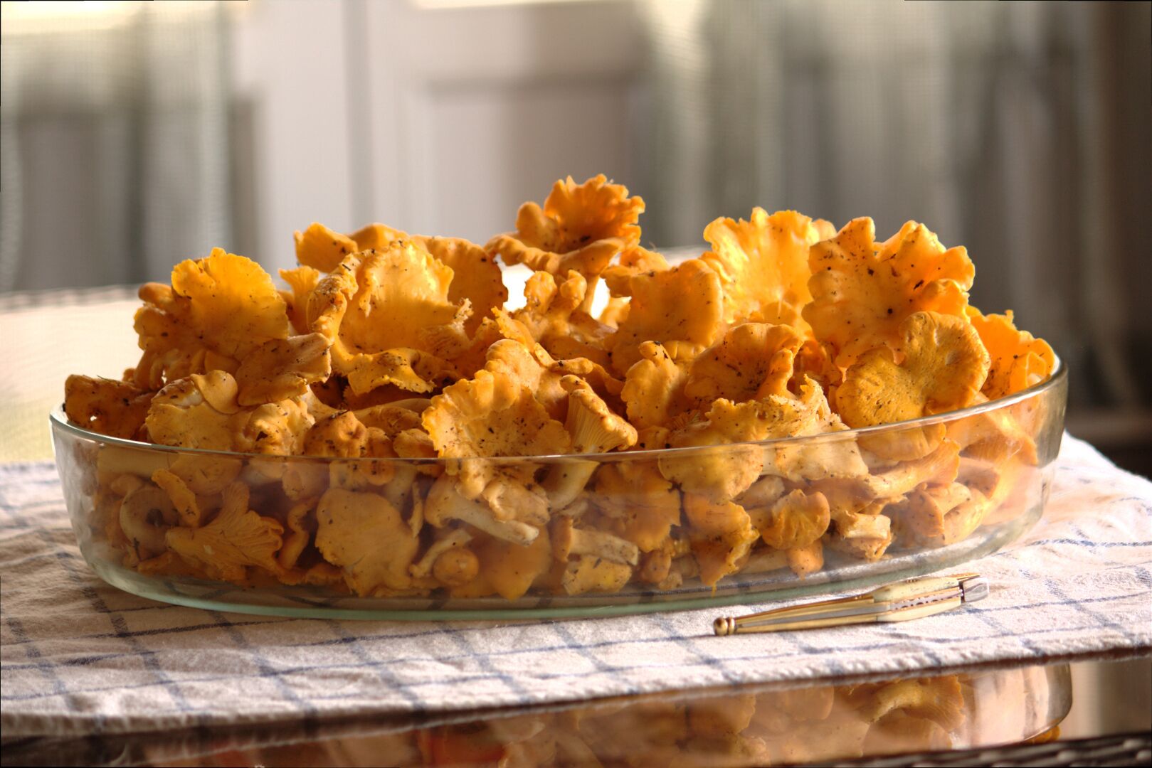A glass bowl filled with seasoned mushrooms on a checkered cloth.