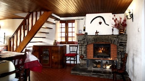 A cozy room with a fireplace, wooden ceiling, and a staircase.