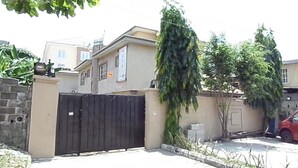 A gated residential area with a beige house, a black gate, and a red car parked nearby. - Cristabol Apartments (Lekki)