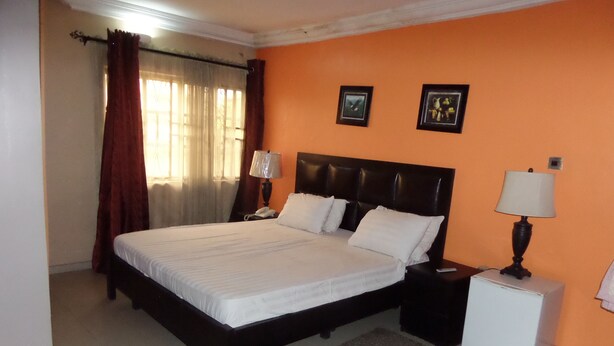 A bedroom with a bed, nightstands, a lamp, a rug, and two framed pictures on the wall. - Cristabol Apartments (Lekki)