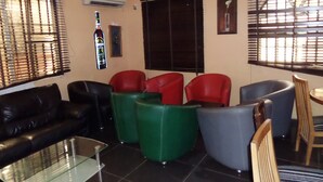A living room with a black leather sofa, green and red chairs, a glass coffee table, and a wooden dining table. - Cristabol Apartments (Lekki)