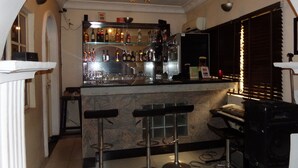 A bar area with a counter, shelves of bottles, and two stools. - Cristabol Apartments (Lekki)
