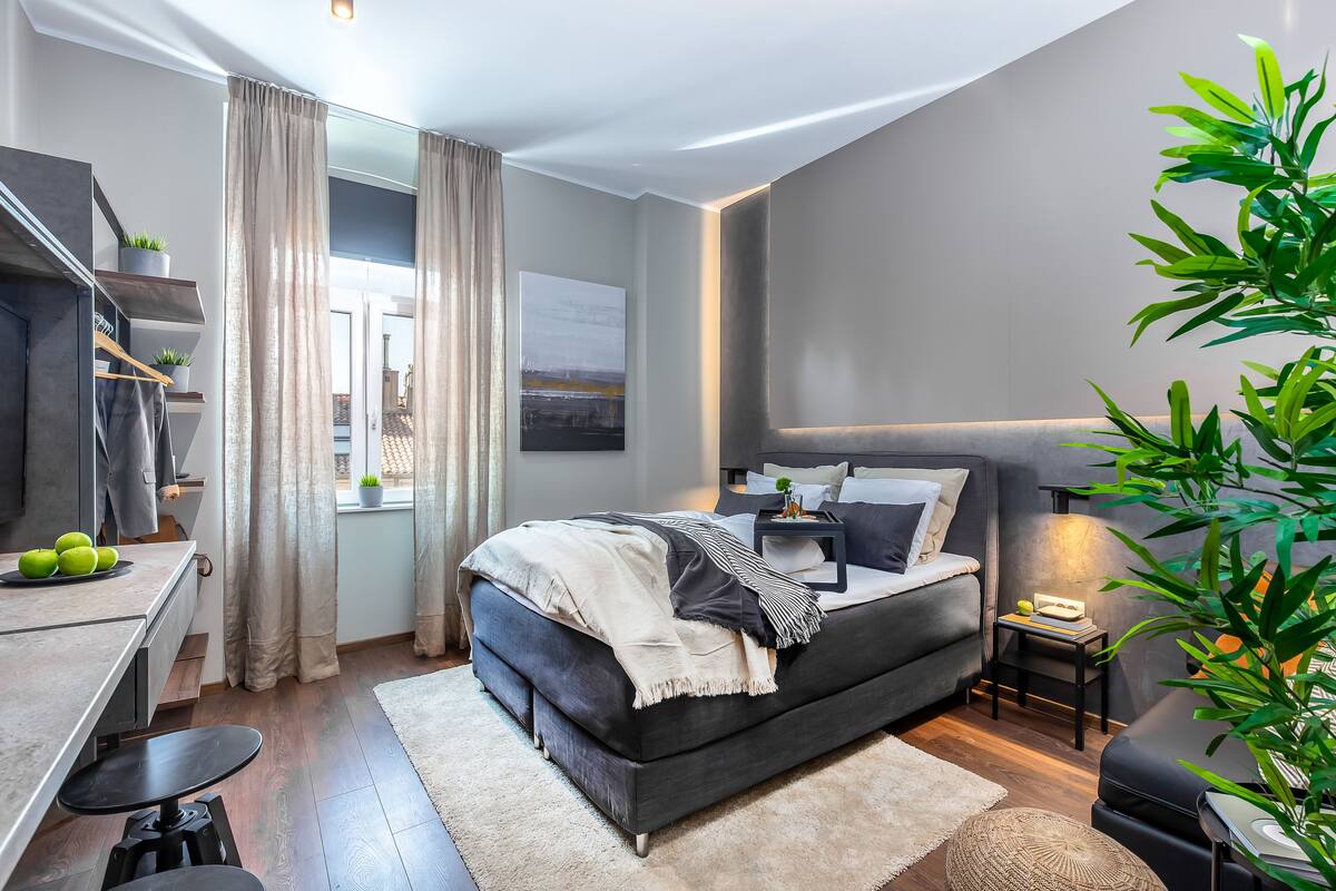 A modern bedroom with a large bed, bedside tables, a desk, and a potted plant.