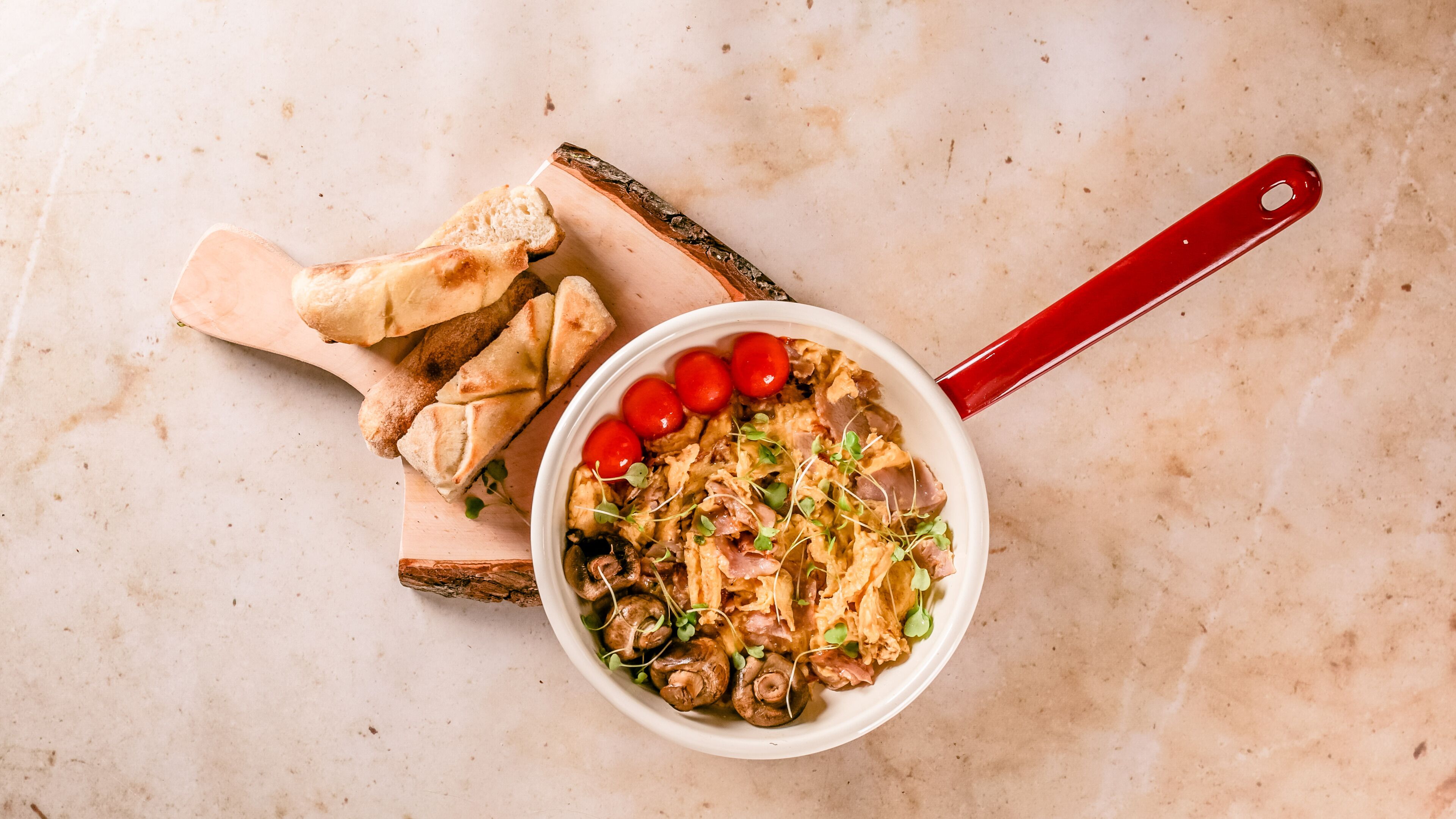 A bowl of food with mushrooms and cherry tomatoes on a wooden board.