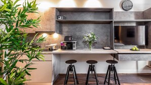 Cocina moderna con microondas integrado, un reloj y un refrigerador de acero inoxidable. Hay dos taburetes y una planta.