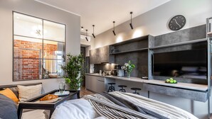 Un espacio habitable moderno y compacto, con kitchenette, una cama con mesita de noche y un ventanal con vista a un muro de ladrillo.