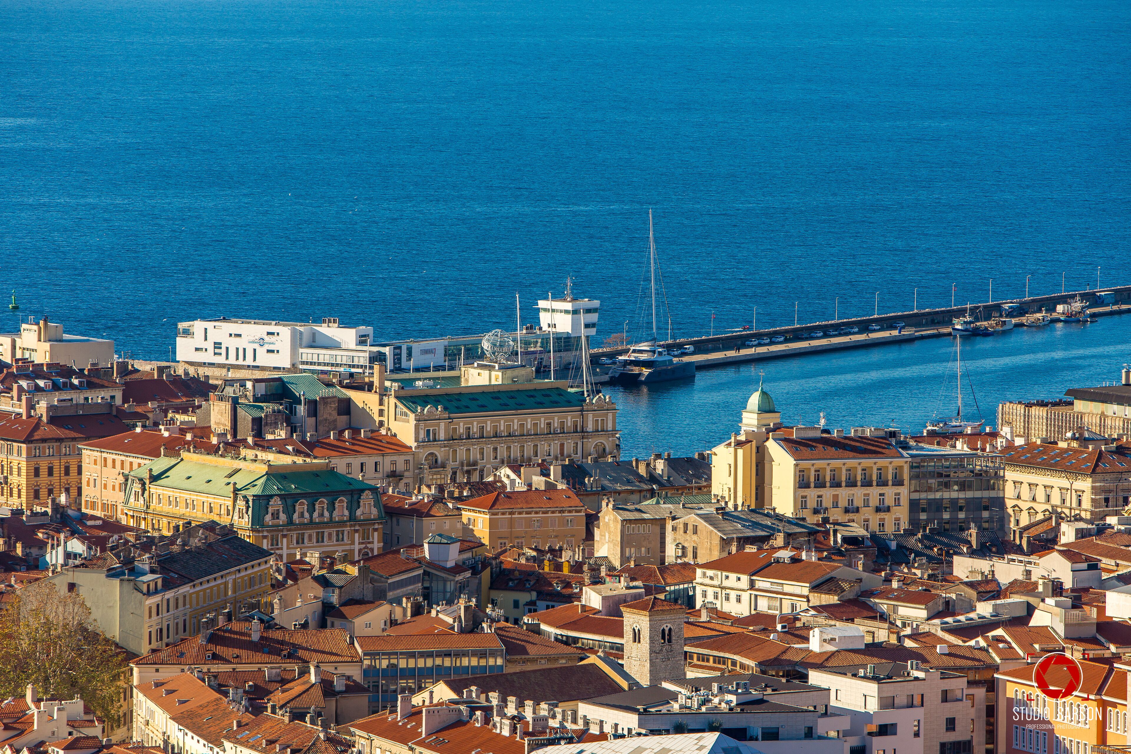 Un paisaje urbano costero con edificios históricos, un puerto deportivo y un puente.