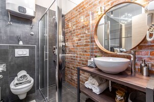A modern bathroom with a glass shower, a white sink, and a brick wall.
