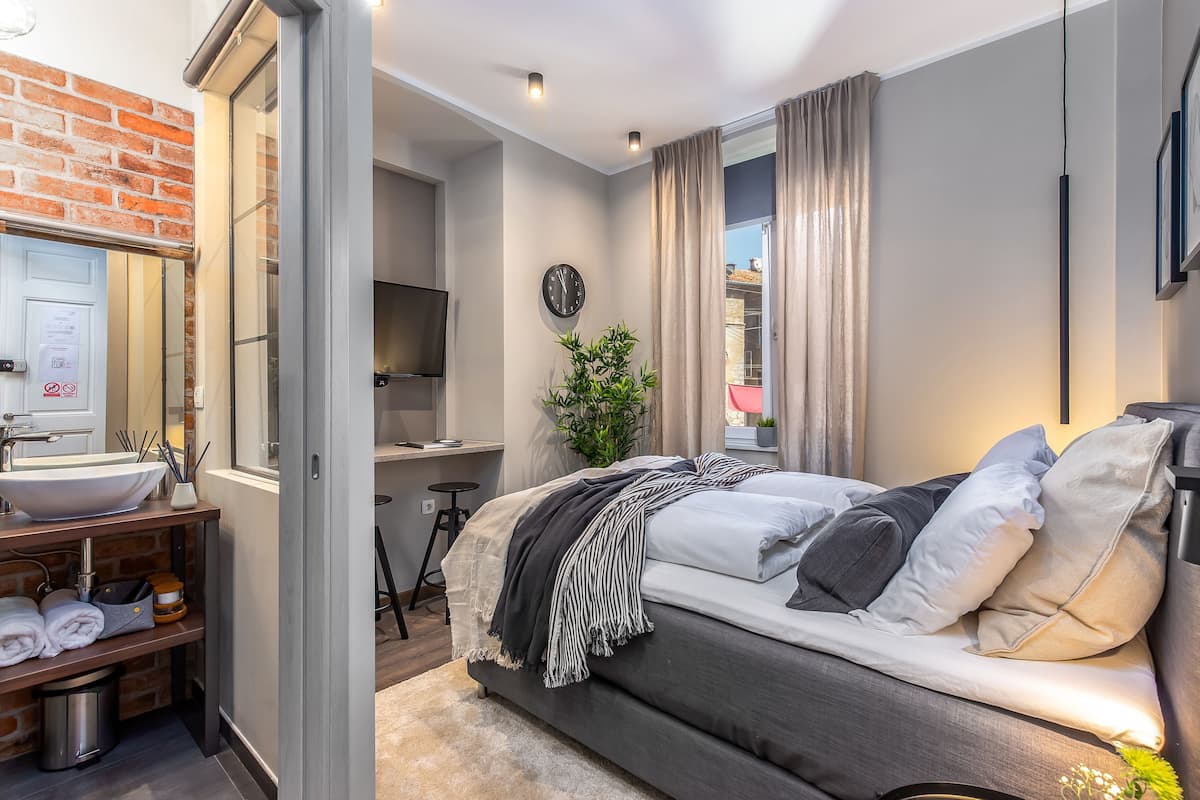 A modern bedroom with a large bed, a bedside table, a mirror, a clock, and a plant.