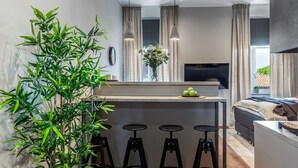 Una cocina moderna con una isla central, taburetes de bar, una planta grande en maceta y un televisor sobre la isla.