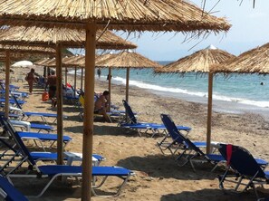 A beach with thatched umbrellas and blue lounge chairs.