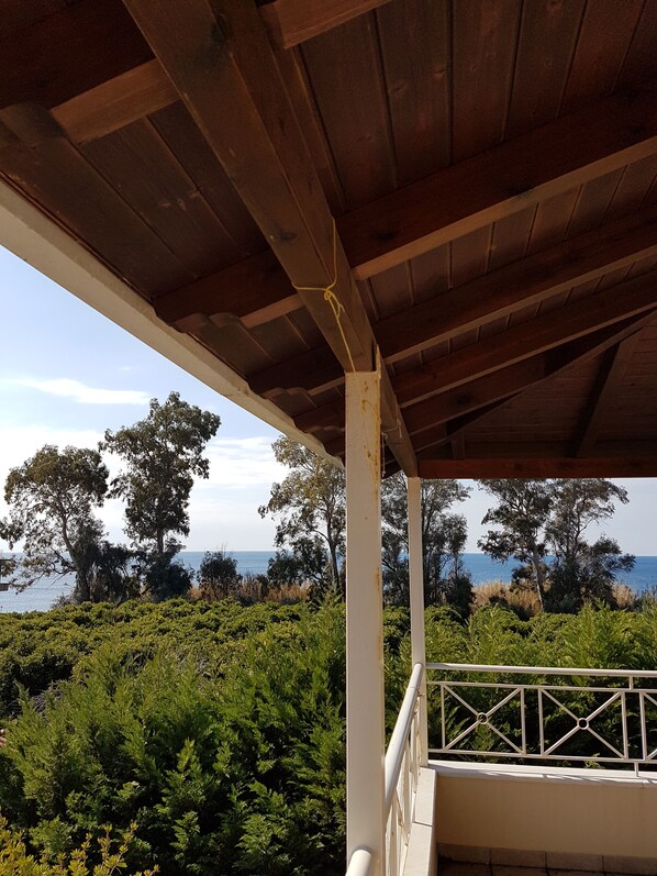 A wooden balcony with a view of the sea and trees.