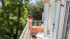 Un balcone con tavolo e sedie, piante in vaso e vista sugli alberi.