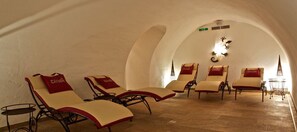 A sunroom with four lounge chairs, each with a red cushion labeled "Crabe." The room has a vaulted ceiling and a wooden floor. - Pension Traube (Uderns)