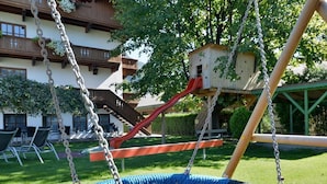 Un patio de juegos con un columpio de cuerda azul, un tobogán rojo y una casita de madera.