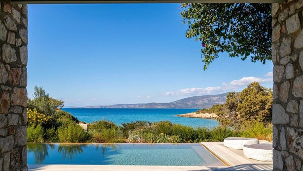 Une piscine à débordement bordée de pierres, offrant une vue dégagée sur la mer et les montagnes lointaines.