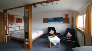 A room with a wooden bed, a small table with a vase, two chairs, and a painting on the wall. - Pension Birgit (Todtnau)