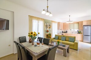 A modern living room with a dining table, chairs, a sofa, and a kitchen in the background.
