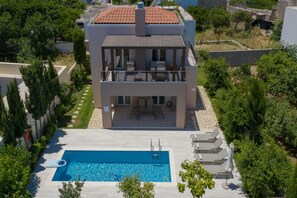 A modern two-story house with a swimming pool, outdoor furniture, and a garden.