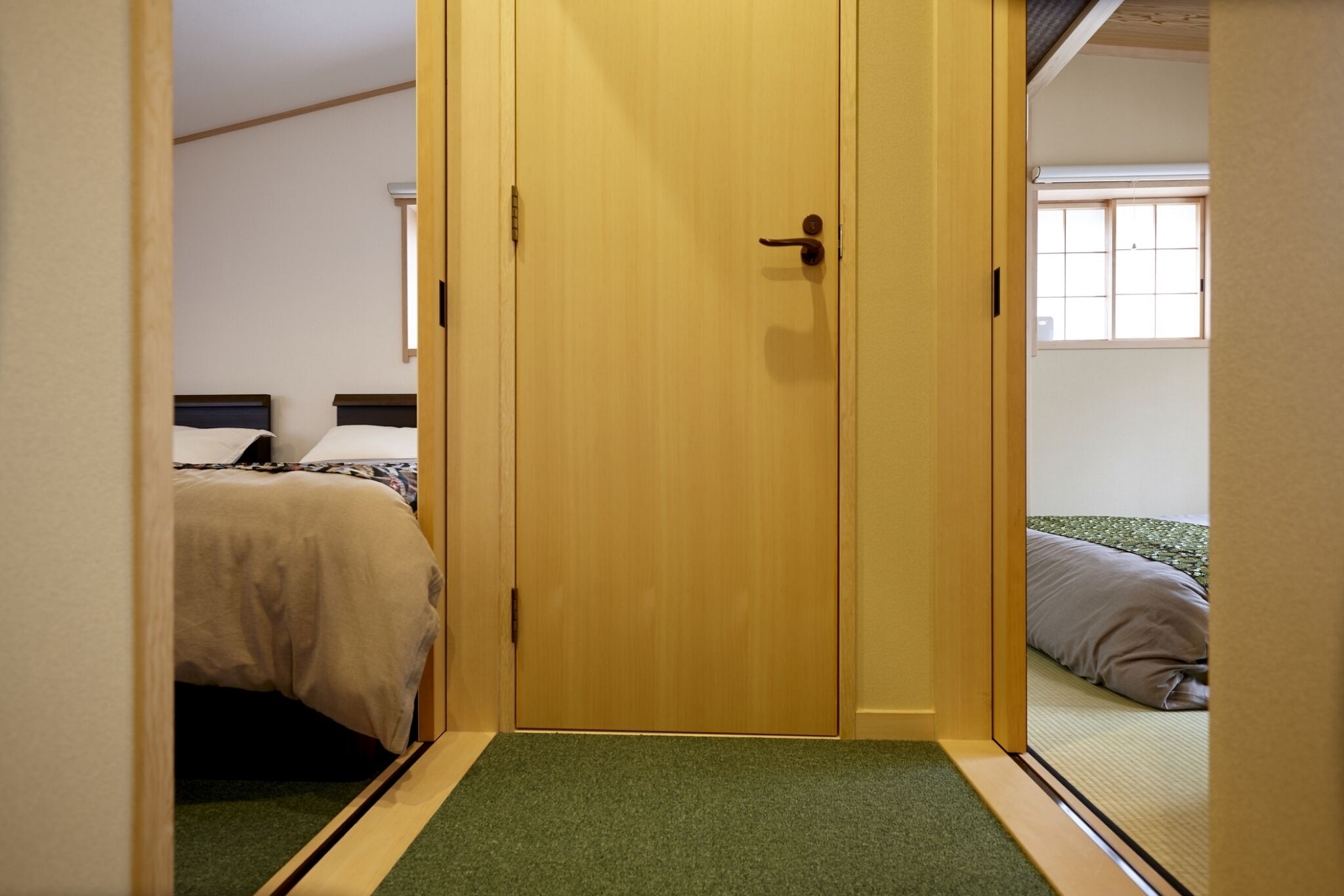 Une pièce avec une porte en bois, un lit recouvert d’un matelas vert et une fenêtre donnant sur un beau paysage.