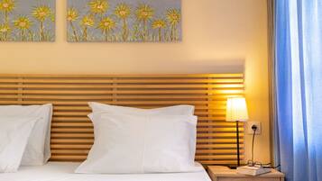 A hotel room with a wooden headboard, white bedding, two white pillows, a bedside table with a lamp, and two paintings of flowers on the wall.