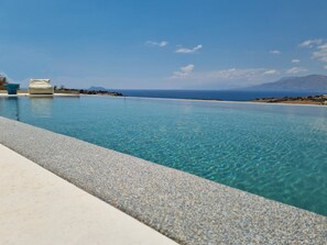 Una piscina infinita de color azul claro con vistas al mar y montañas distantes.