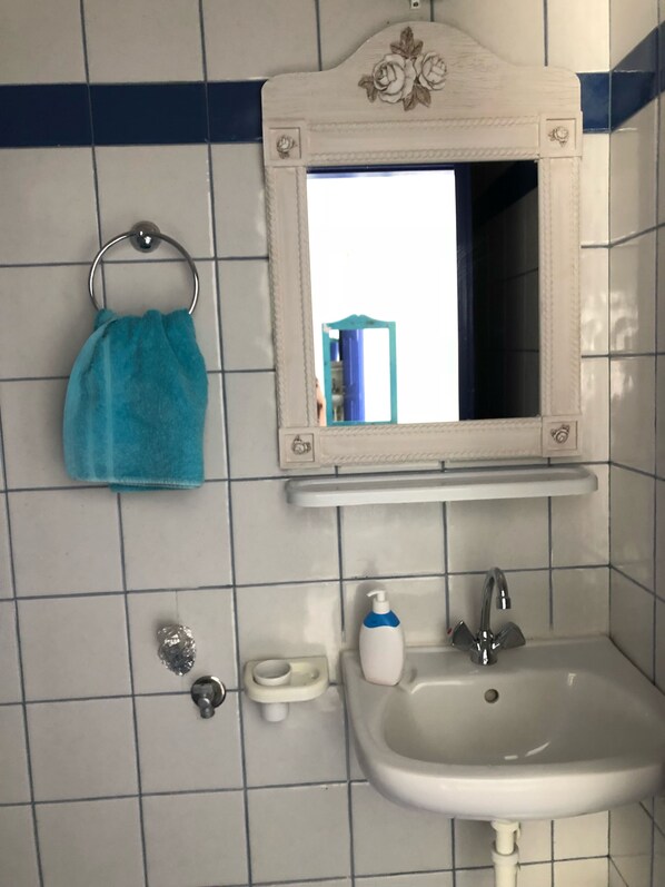 A bathroom with a white sink, a mirror with a floral frame, a towel rack with a blue towel, and a soap dispenser. - Villa Grabella Amazing sea view and swimming pool (Πιτσίδια)
