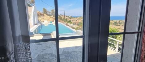 A view through a window with a pool and stone patio.