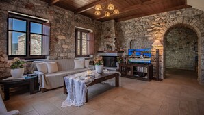 Een gezellige woonkamer met stenen muren, een houten plafond, een bank, een salontafel en een televisie.