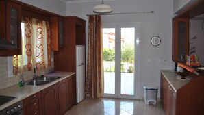A kitchen with a sink, cabinets, a refrigerator, and a trash bin. - VILLA ANDREAS Family- friendly & friends- friendly (Καραβόμυλος)