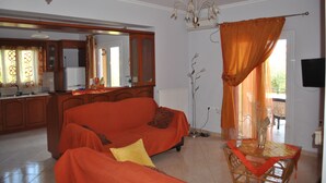 A living room with a sofa, a dining table, a chandelier, and a kitchen area. - VILLA ANDREAS Family- friendly & friends- friendly (Καραβόμυλος)