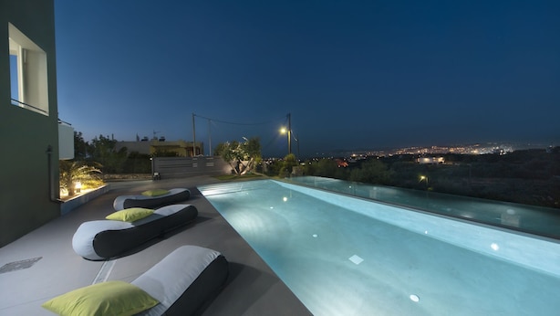 Ein moderner Poolbereich im Freien mit Liegestühlen und Blick auf die Stadt bei Dämmerung.