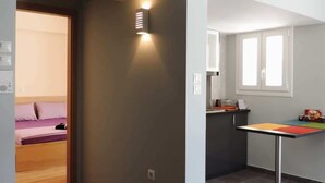 Um interior moderno com área de cozinha, uma mesa de jantar e um quarto visível por uma porta aberta.