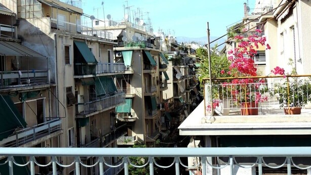 Uma rua estreita no centro da cidade, com edifícios altos e bem próximos, sacadas e antenas parabólicas.