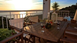 A wooden table with two wine glasses and a bottle, set on a balcony overlooking a body of water at sunset. - Malena Pool Villa  with stunning view in a quiet location. Free WIFI and jacuz (Γλώσσα)