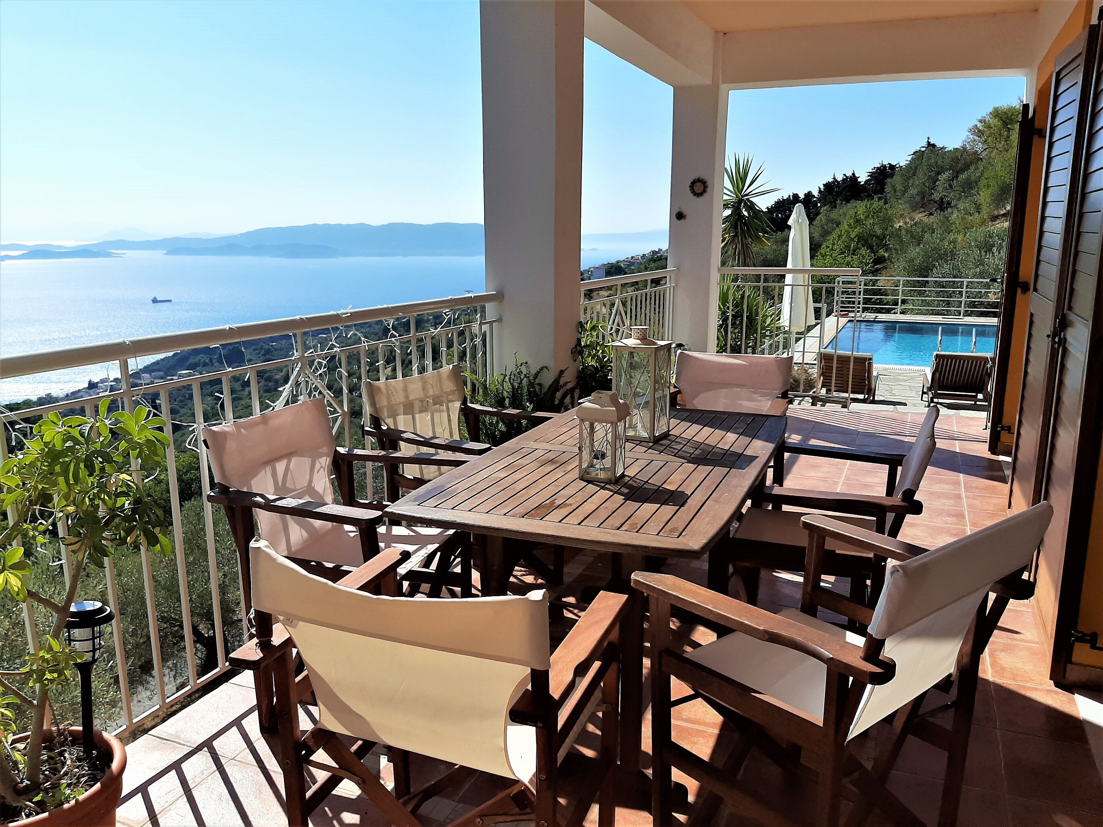 A balcony with a wooden table and chairs, a view of the sea, and a pool.