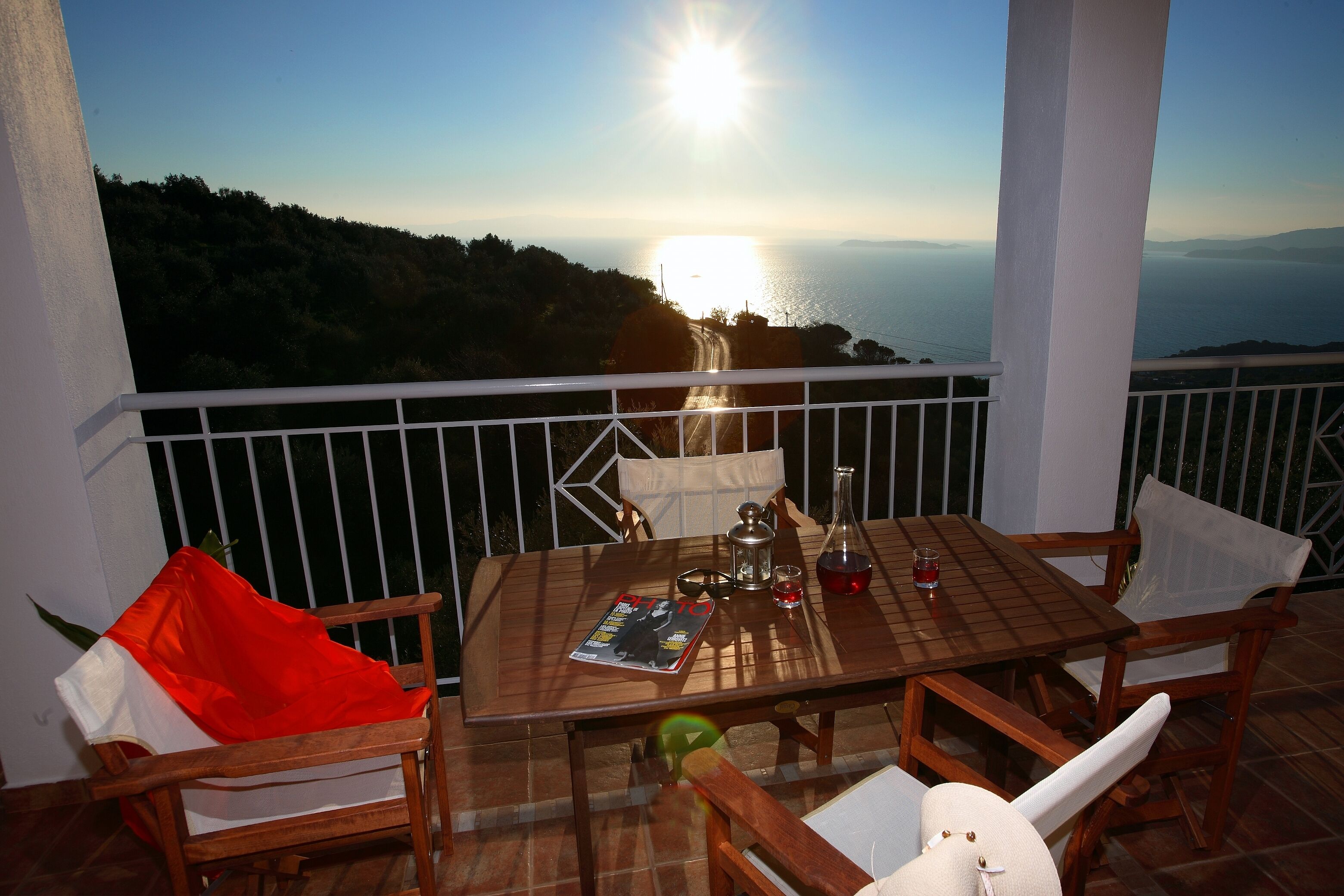 A wooden table with chairs on a balcony overlooking a scenic view of the sea and hills.