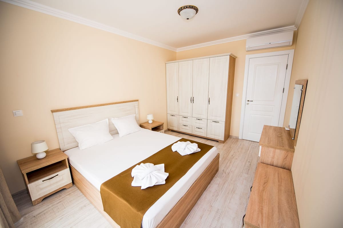 A hotel room with a large bed, wooden nightstands, a wardrobe, and a mirror.