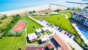 Vista aérea de uma área costeira com quadra de tênis, estacionamento e edifícios.