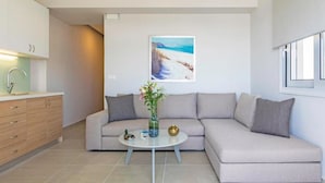 Una sala de estar moderna con un sofá beige, una mesa de centro redonda y un cuadro de una playa.