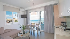 Una sala de estar moderna con un sofá, una mesa de comedor con sillas, una pequeña mesa de centro con una planta y un televisor montado en la pared.