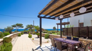 Un espace patio avec une table et des chaises, une pergola agrémentée de guirlandes lumineuses et une vue sur la mer.