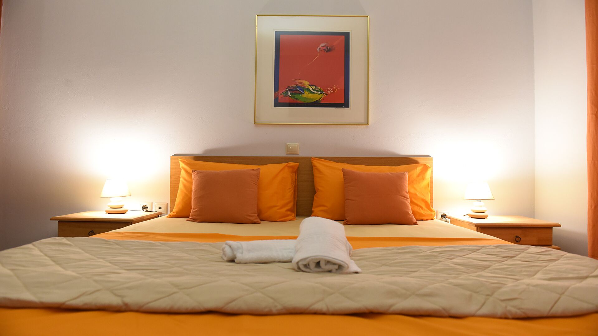 A hotel room with a bed, two nightstands, two lamps, and a framed picture on the wall.