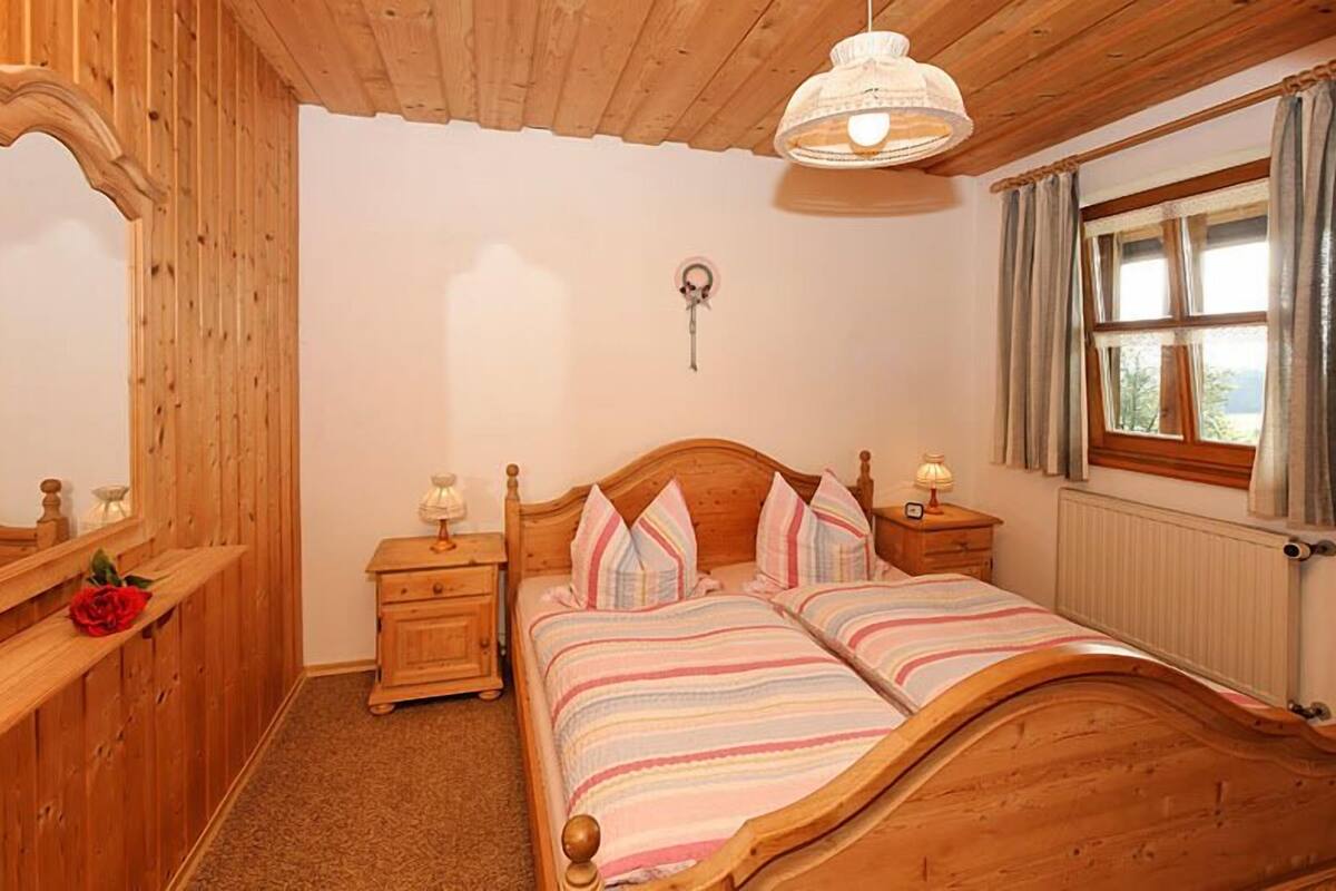A wooden bedroom with a bed, nightstands, a mirror, and a window with curtains.